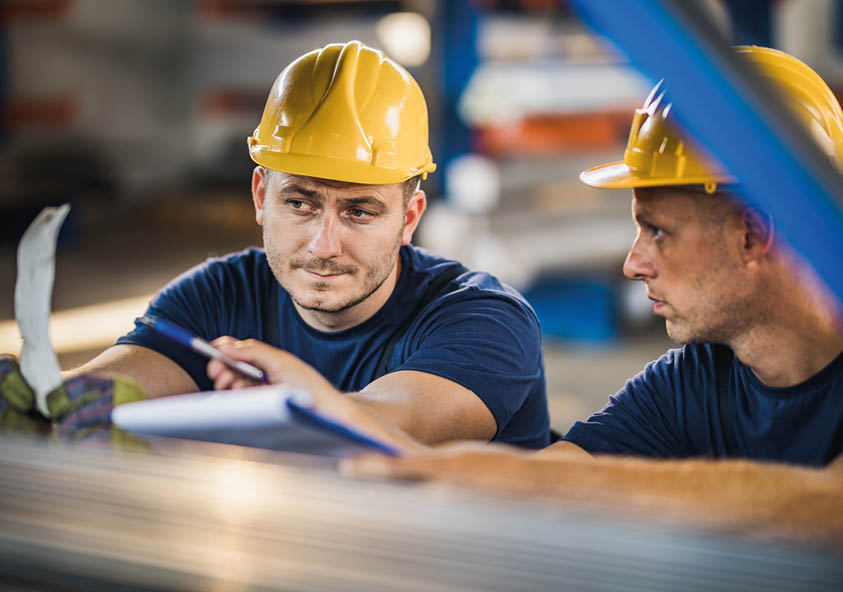 Two manual workers cooperating while working on reports in steel mill.